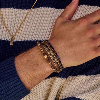 Handgelenk mit mehreren Armbändern, darunter ein goldener Stahlarmreif, vor gestreiftem Pullover.